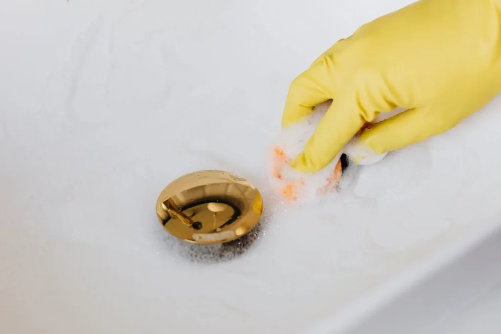 Gloved hand cleaning a sink drain, near the most common water leak in a house